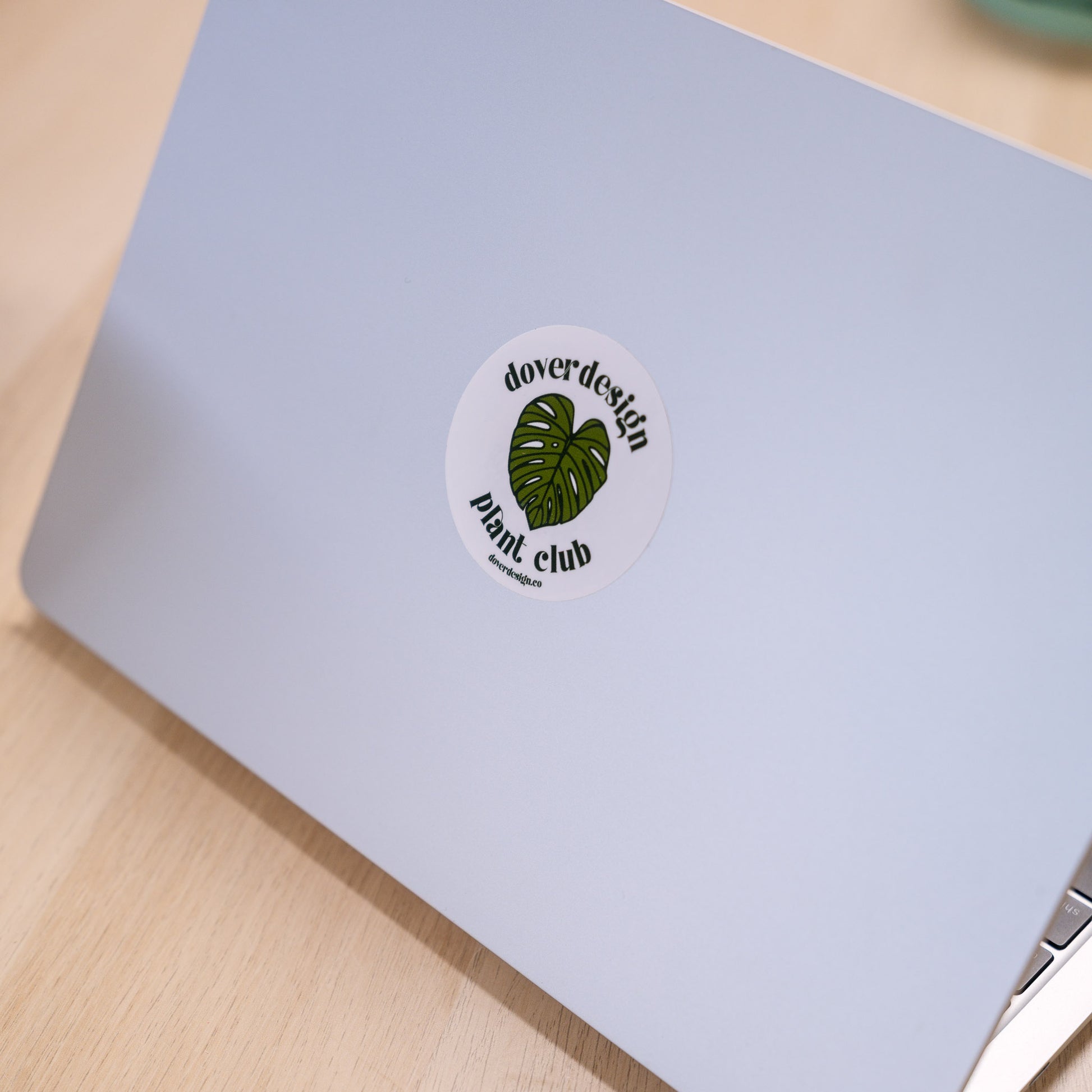 Laptop with a Dover Design Plant Club sticker on a wooden surface