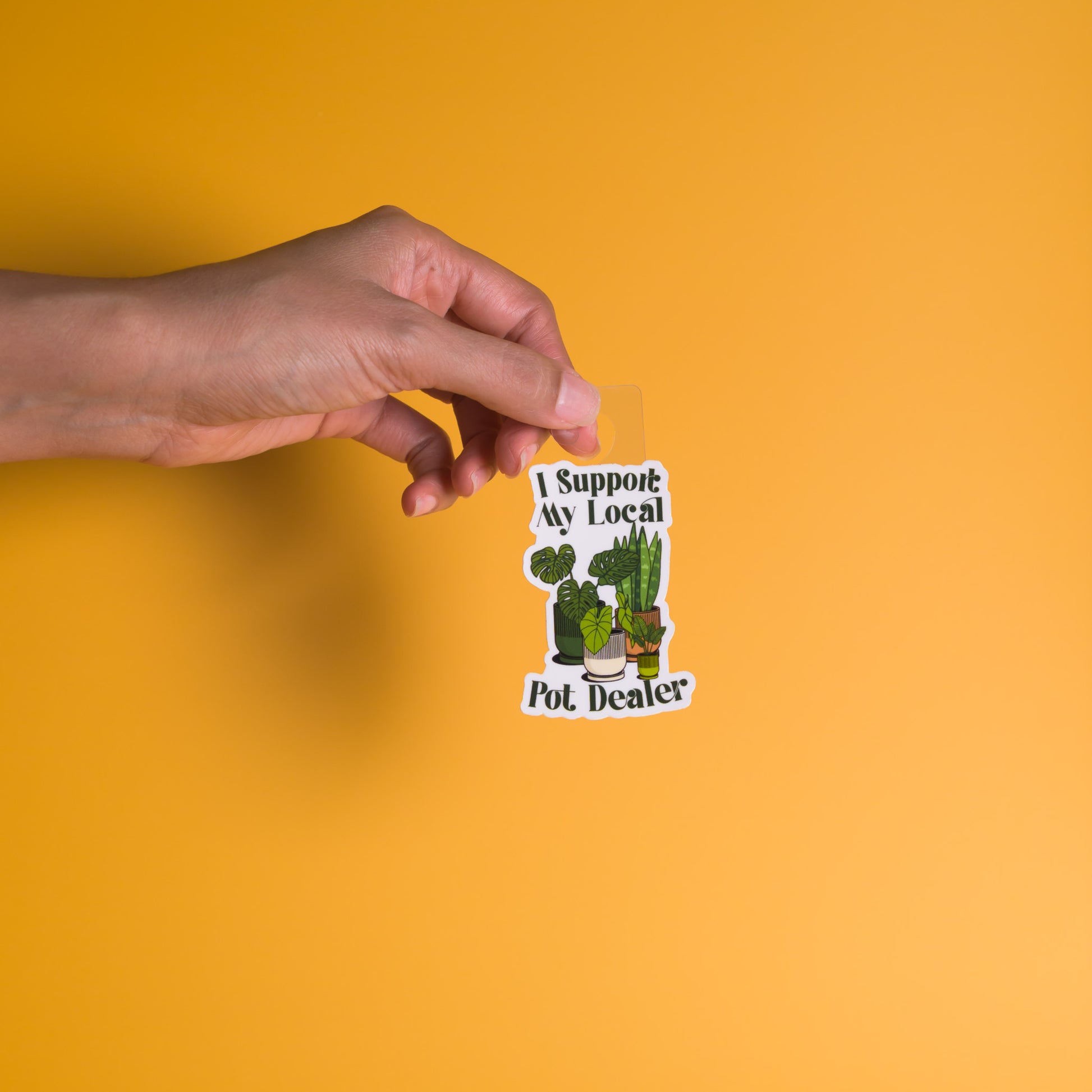 Hand holding a sticker with cactus illustrations and text on a yellow background