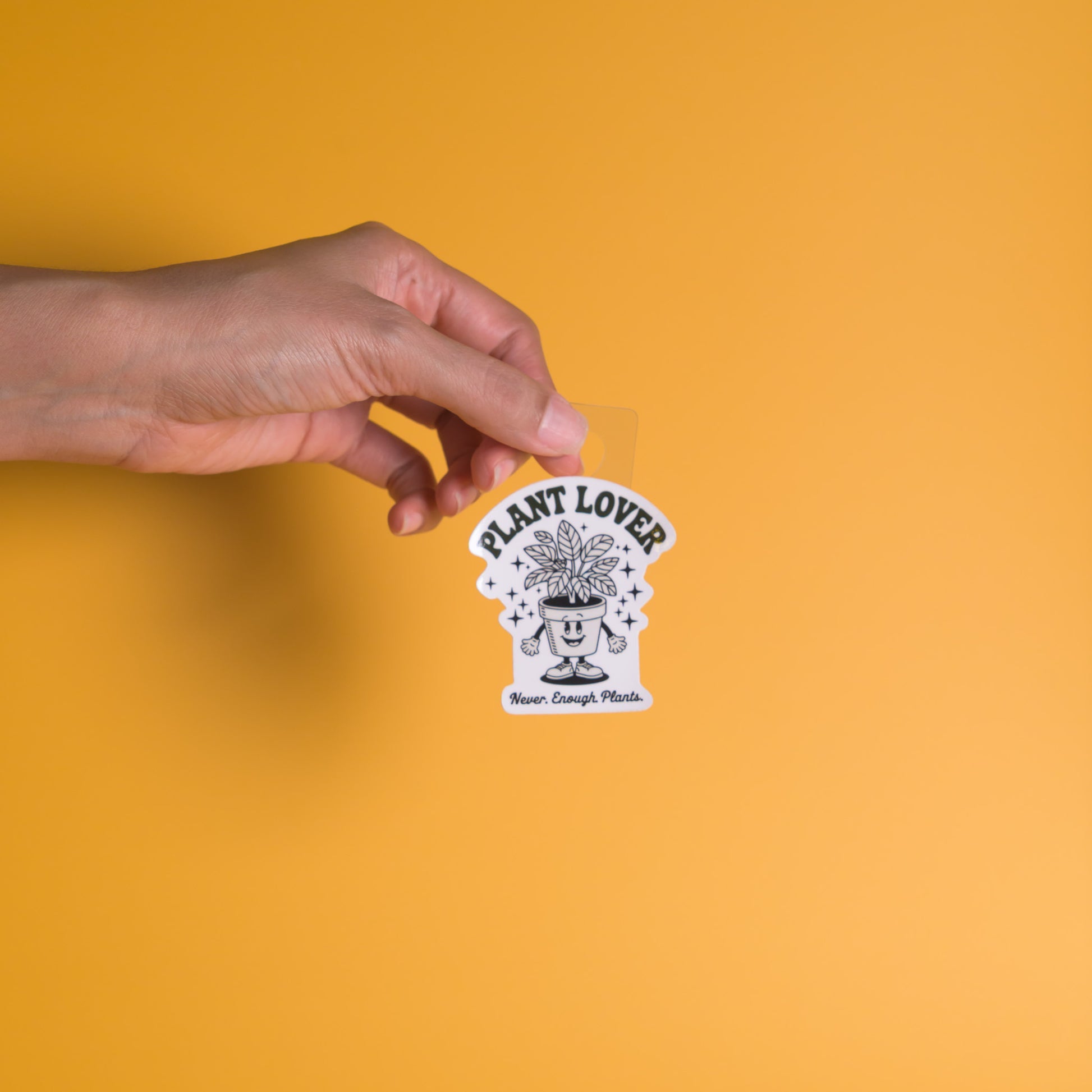 Hand holding a 'Plant Lover' sticker against an orange background