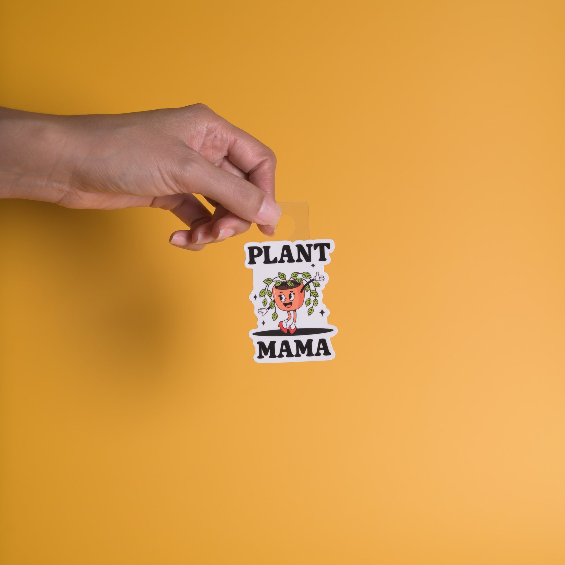Hand holding a 'Plant Mama' sticker against an orange background